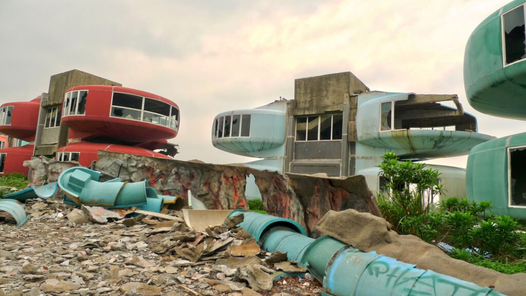Faded red and yellow Futuro-style houses surrounded by greenery in an overgrown complex.