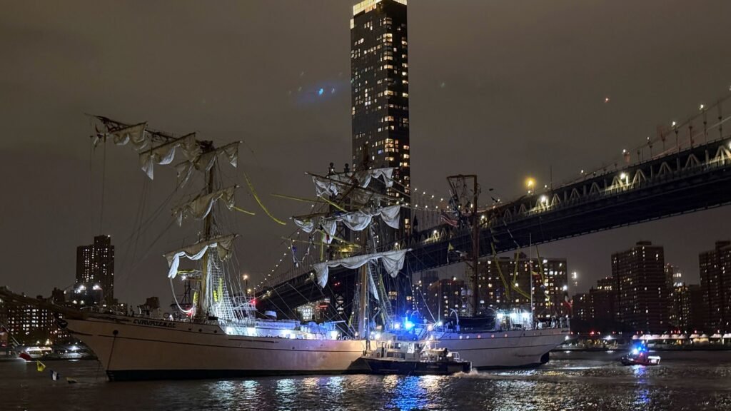 The Mexican Navy training vessel Cuauhtémoc with a tugboat assisting it near the Brooklyn Bridge at night, showing its impressive size before the collision that occurred on May 17, 2025.
