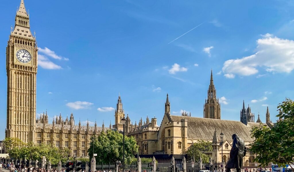 Parliament Square in London, United Kingdom, showcasing Big Ben, the Houses of Parliament, and surrounding statues under a bright blue sky.