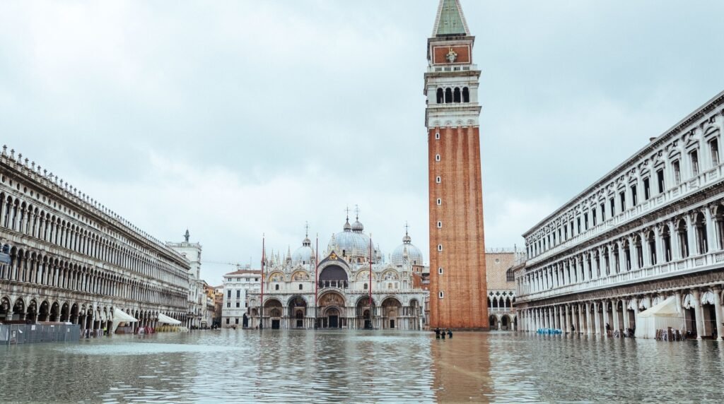 Wide view of Venetian flooding as a shallow lagoon engulfs St Mark’s Basilica and the Campanile, revealing the full extent of the high-tide surge in the historic square.