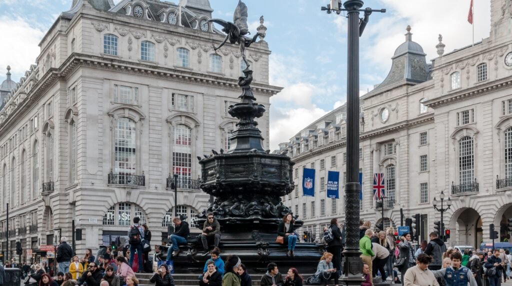 Piccadilly Circus in London, United Kingdom, featuring the famous Eros Fountain, historic buildings, and crowds of people in a lively urban scene.