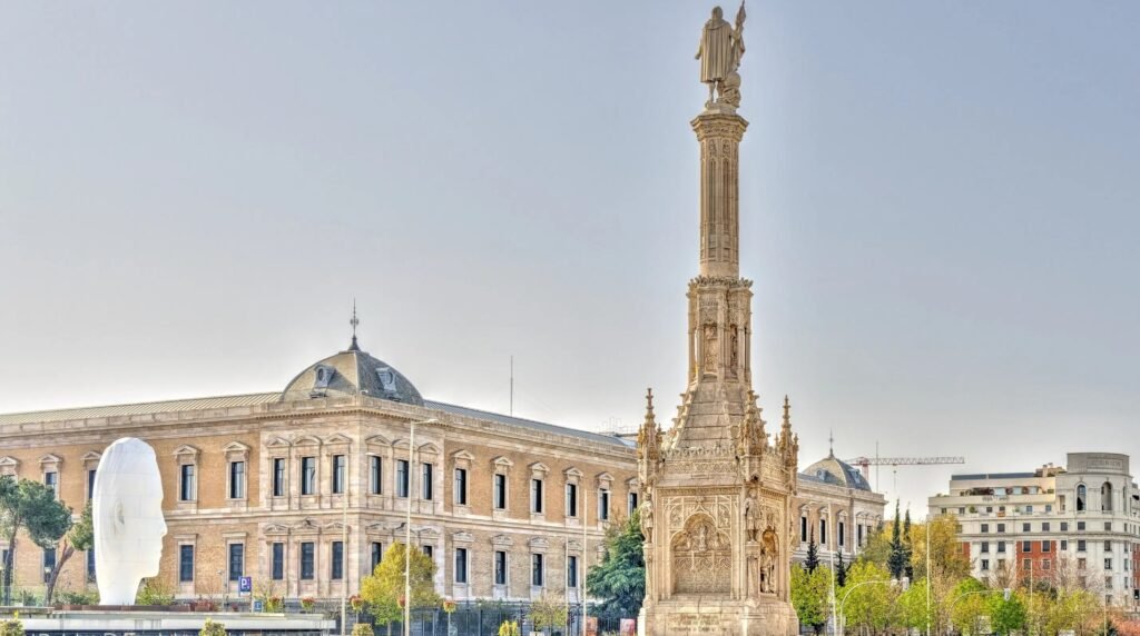 Plaza de Colón in Madrid, Spain, featuring the grand Columbus monument and surrounding neoclassical buildings under a clear sky.