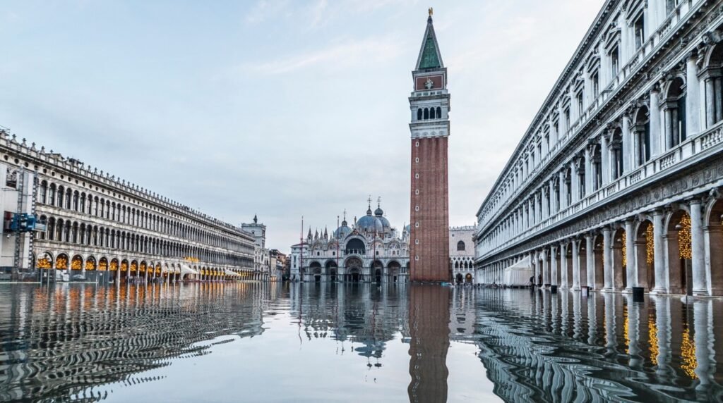 Piazza San Marco reflected like a mirror during early-morning high water, the Campanile di San Marco towering above silent, floodlit arcades.