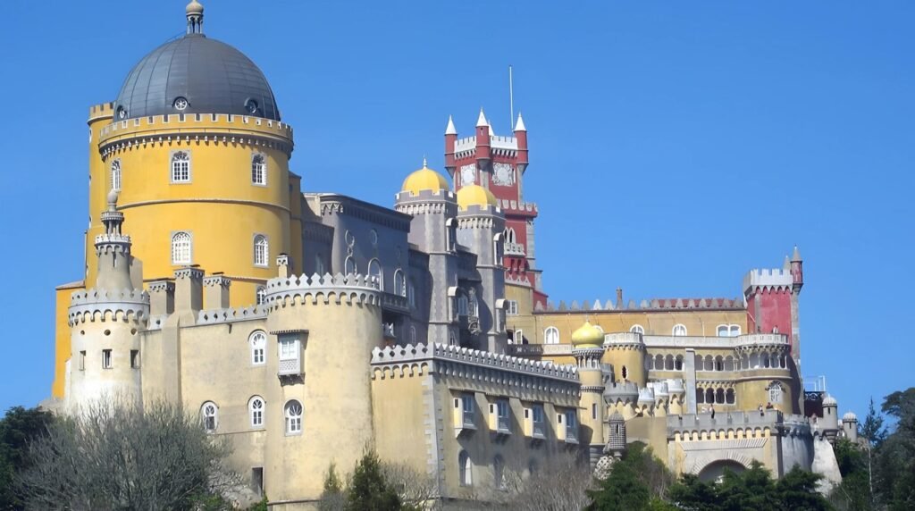 A brightly colored castle with yellow and red towers, a grey dome, and numerous windows, set against a clear blue sky.
Pena Palace, Sintra, Portugal