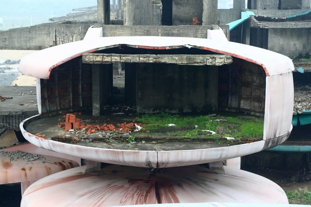 Interior view of a yellow pod showing decayed furniture and peeling walls through a broken window.