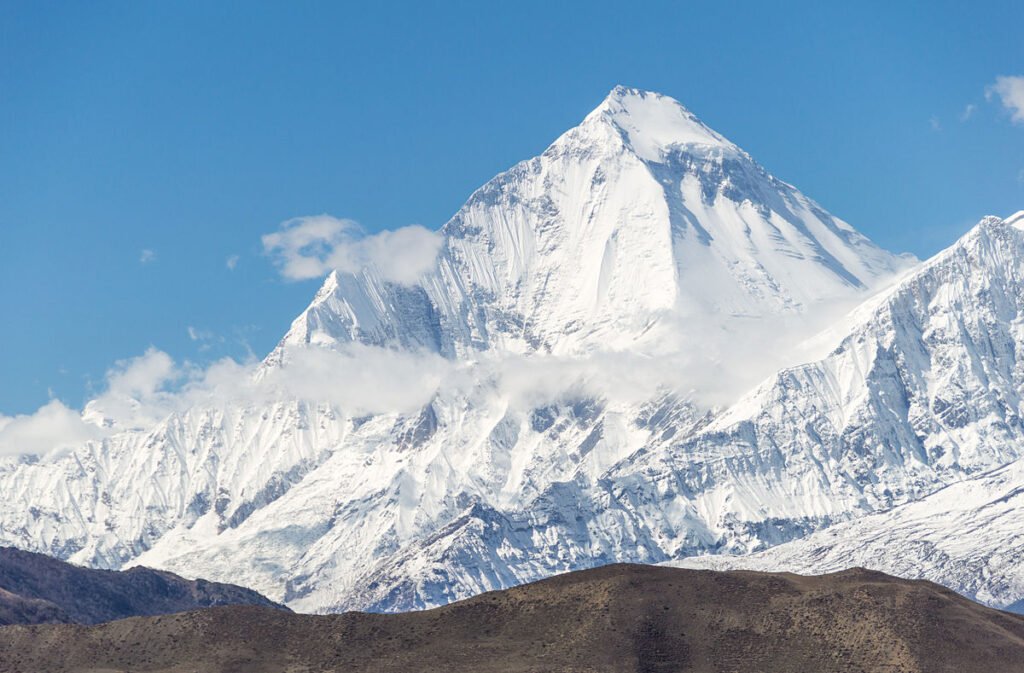 Dhaulagiri I, the seventh highest mountain on Earth at 8,167 meters, showing a snow-covered peak under a bright blue sky, located in Nepal.