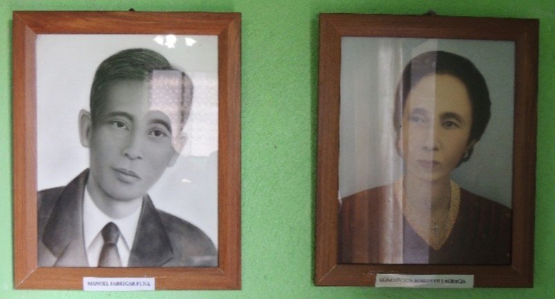 Two framed, black-and-white portraits hang side-by-side on a green wall: one of a distinguished man named Manuel Barrio Funa, and the other of Concepcion Barrios Valencia.