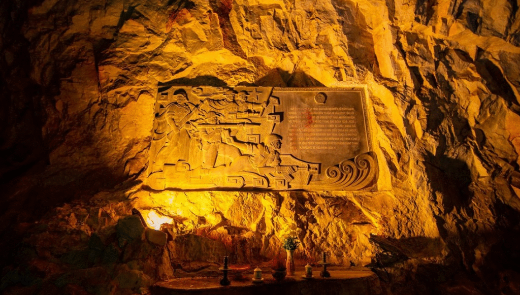 A stone bas-relief inside a cave depicts soldiers in action, with text on the right. The entire scene is bathed in a warm, golden light emanating from below.