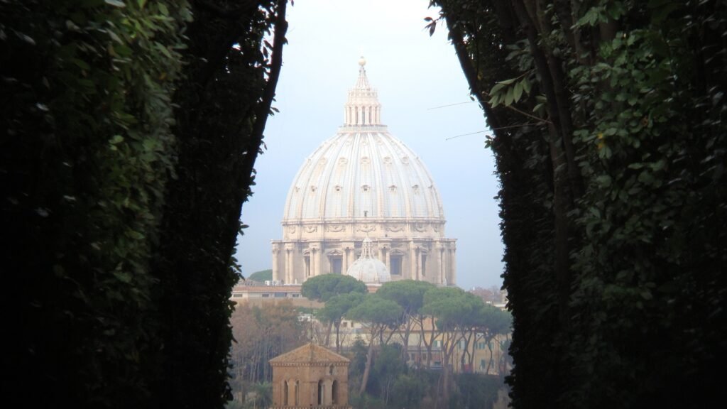 View of St. Peter’s Basilica dome perfectly framed by the leafy green keyhole tunnel of the Aventine Hill gardens in Rome.