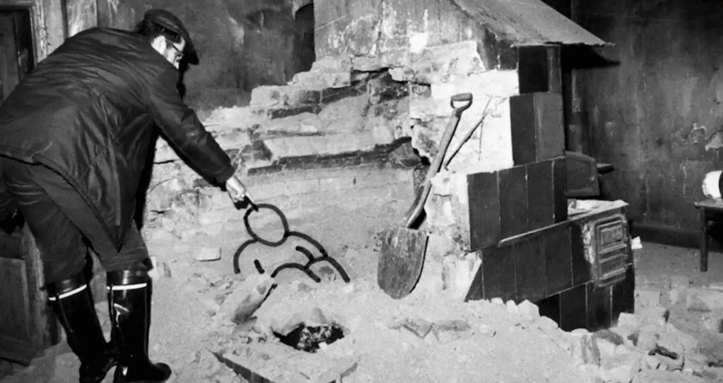 A historical black and white photo showing an investigator pointing to the human remains outline found within the rubble of the demolished brick oven in the Saarinen home.
