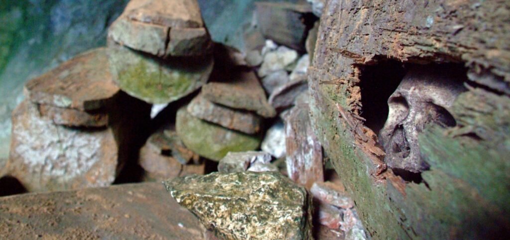 A partially decayed wooden coffin showing a human skull inside, part of the hanging coffins burial tradition in the Philippines.
