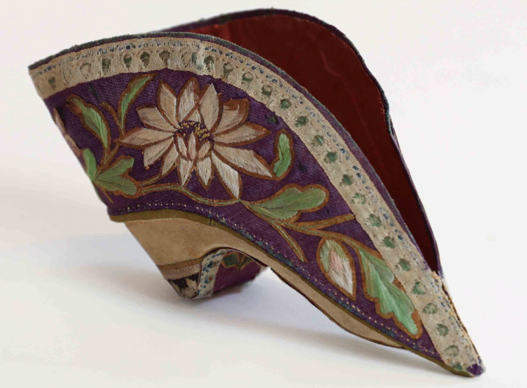 A vibrant purple embroidered "lotus shoe" for Foot Binding China , featuring a prominent lotus flower design, illustrating the small, pointed footwear used in this historical practice.