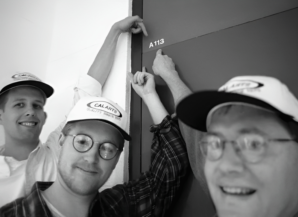 CalArts students smiling and pointing at the famous classroom door labeled “A113,” known for inspiring Pixar’s Easter egg.