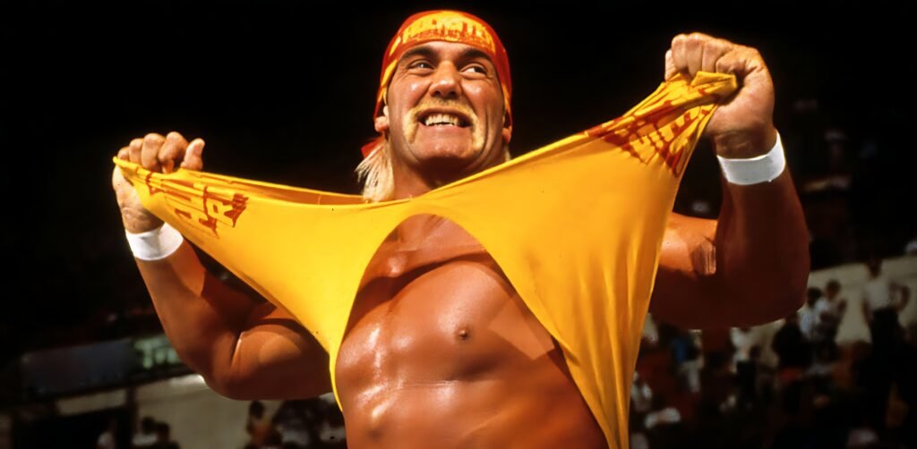Hulk Hogan in his classic red and yellow "Hulkamania" gear, flexing his muscles as he rips his yellow T-shirt, one of his signature taunts.