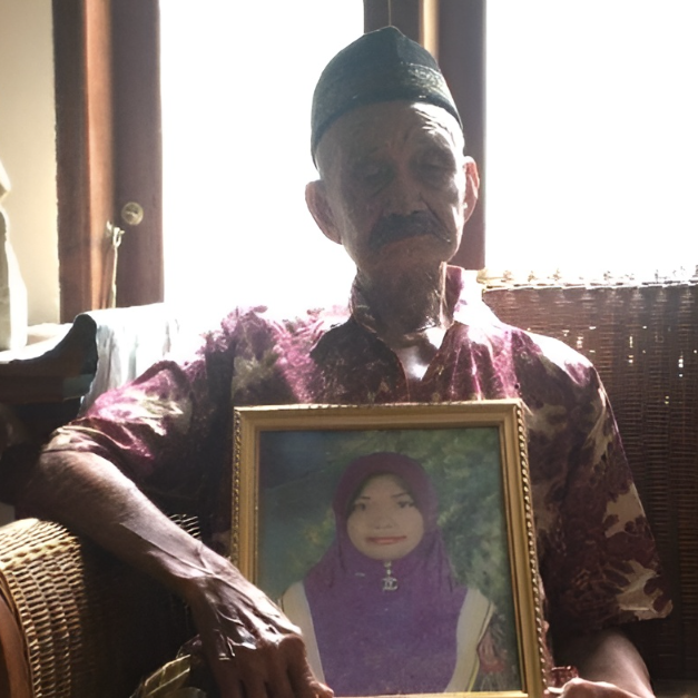 An older man, likely a family member, holding a framed photo of Noor Afiyah Daeng Damin, remembering her life.